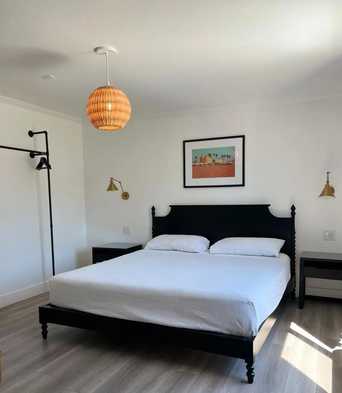 A neatly made bed with white linens in a room with white walls and a pendant light.